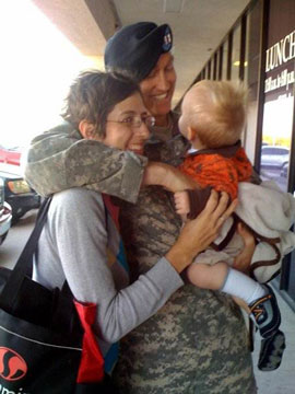 Military service member in uniform hugging two young children indoors at what appears to be a clinic or medical facility.