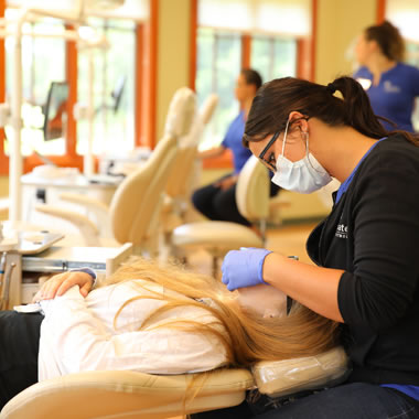 Orthodontist wearing mask and gloves examining patient's dental model in clinical setting.
