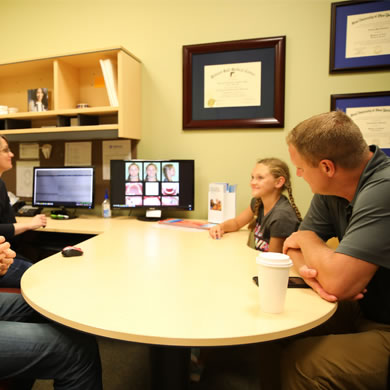 Orthodontist consulting with patients at round table in modern dental office during treatment discussion.