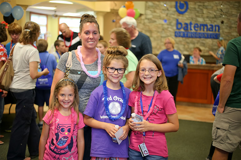 Woman with three children smiling at Bateman Orthodontics event with balloons and attendees in background.