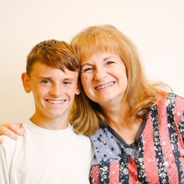 Woman and young boy smiling together for portrait against neutral background.