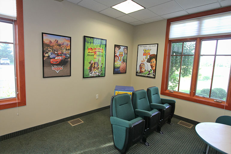 Orthodontic office waiting room with theater seating, Pixar movie posters, and windows overlooking landscaping.
