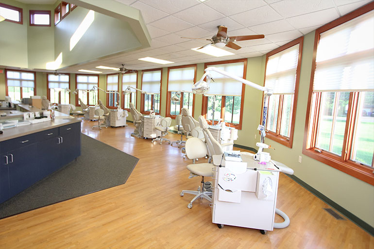Modern orthodontic treatment room with multiple dental chairs, equipment, and large windows in bright clinical setting.