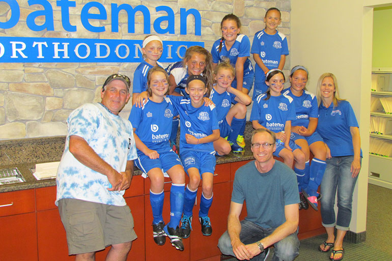 Youth soccer team in blue uniforms posing with coaches at Bateman Orthodontics office.