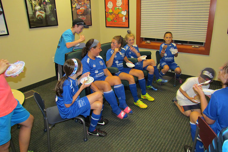 Young soccer players in blue uniforms eating pizza indoors after practice or game.