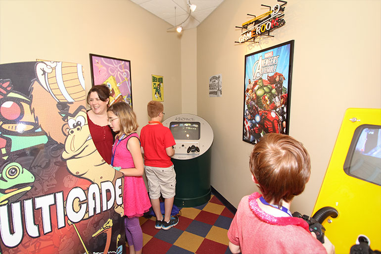 Children playing arcade games in colorful retro video game room with vintage posters.