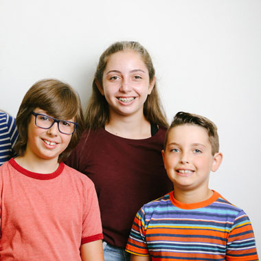 Three smiling children posing together against a white background for an orthodontics practice portrait.