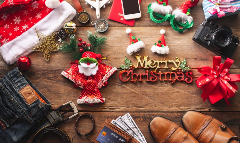 Festive Christmas flat lay with decorations, gifts, camera, and shoes on wooden surface.