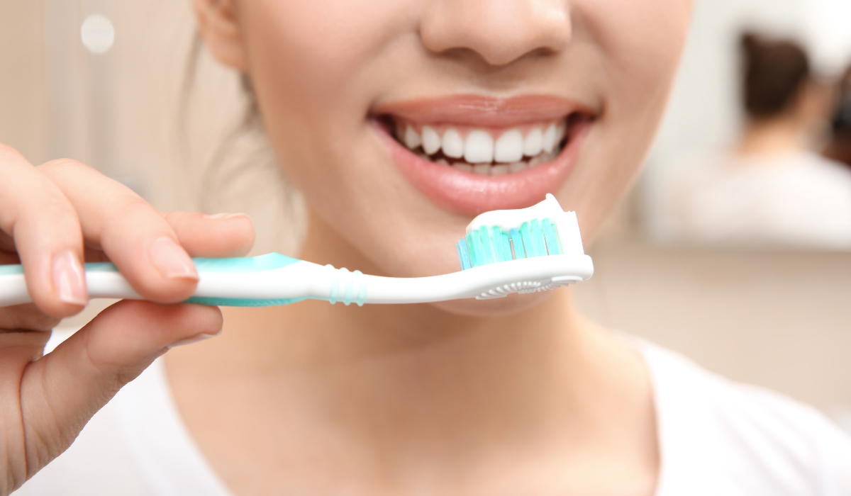 Woman holding a toothbrush with a bright smile demonstrating daily oral hygiene care.