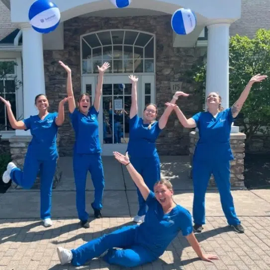 Bateman Orthodontics team in blue scrubs celebrating outside their office building with arms raised.